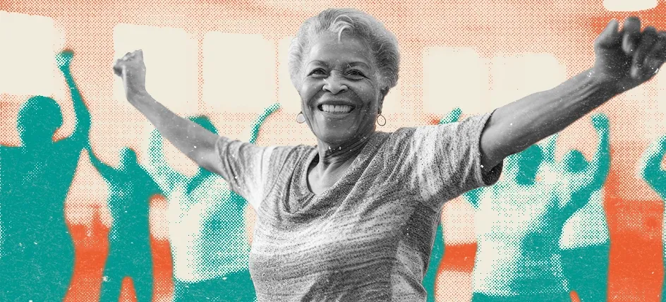 Smiling older woman exercising in a group fitness class, raising her arms with others in the background.