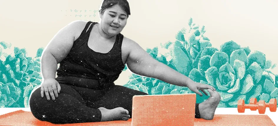 Woman stretching on a yoga mat while following an online workout on a laptop, in a living room with a couch, books, and dumbbells in the background.