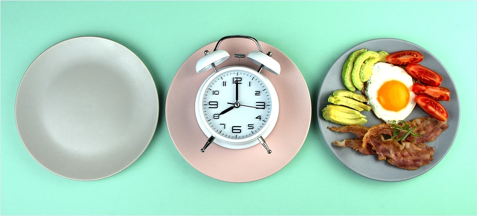 Three plates one empty, one with a clock, and one with food. Representing the choice of fasting before a blood draw.
