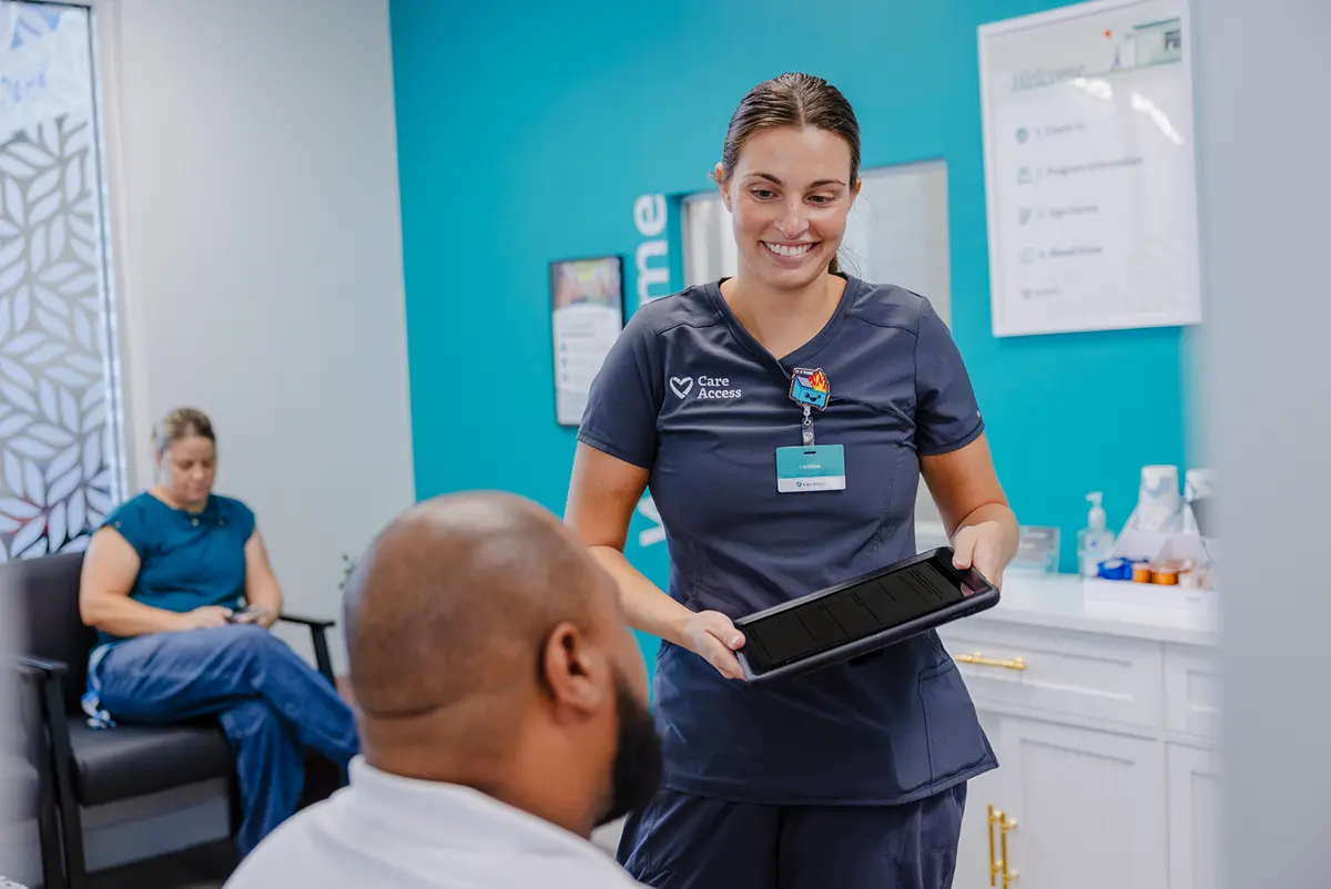 A smiling Care Access team member shows a tablet to a participant in a clinic waiting room