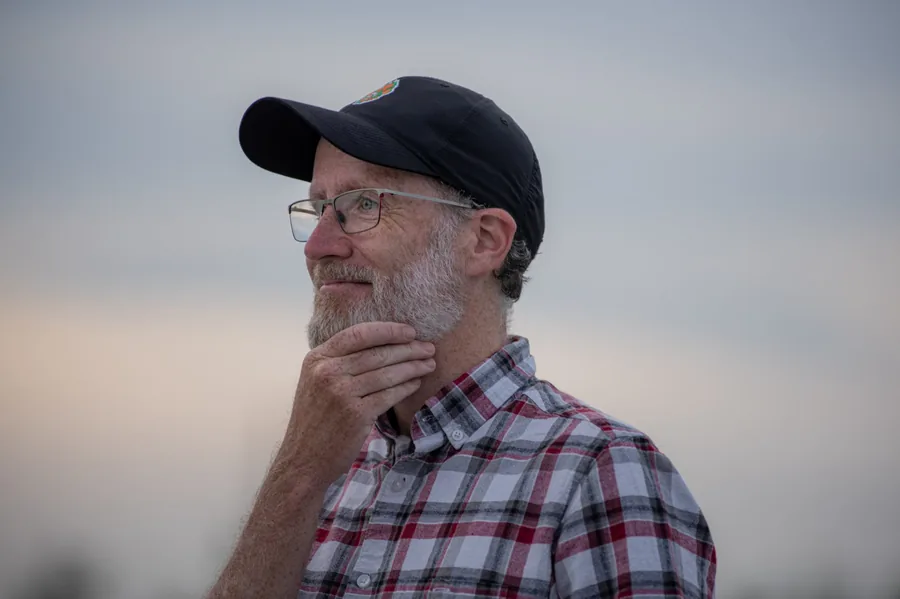 A man in a baseball cap and glasses looking into the distance