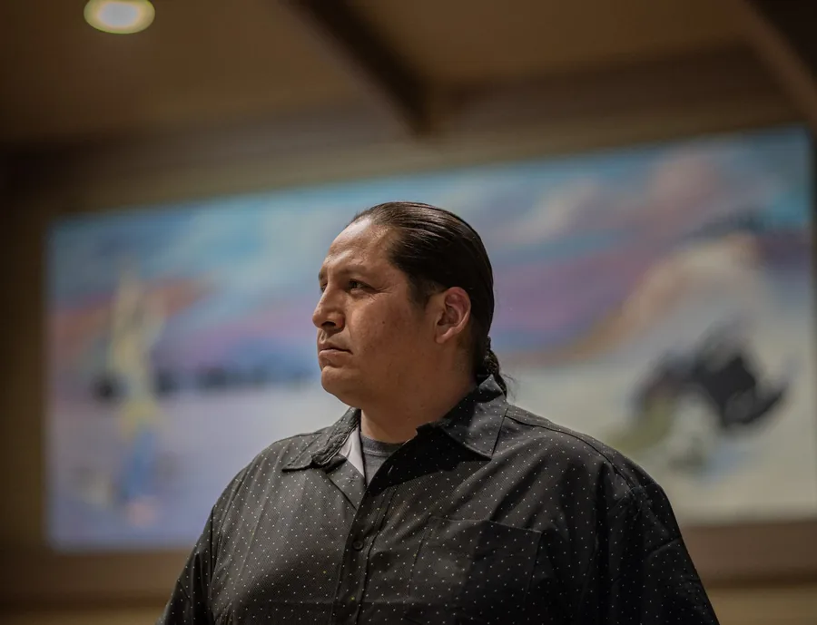 A man with long dark hair in front of a painted mural
