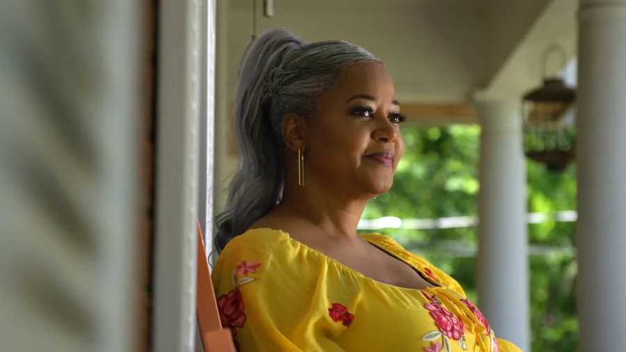 A woman in a yellow patterned dress standing on a porch