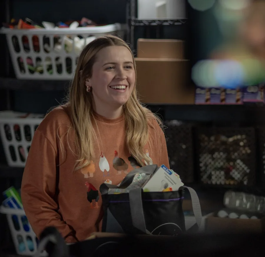 A smiling woman with a tote bag in a shop aisle